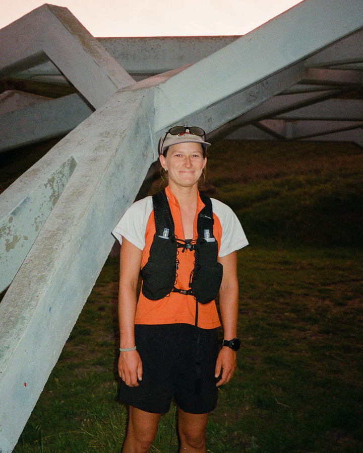 Person wearing an orange vest and black shorts standing under a large metal structure.