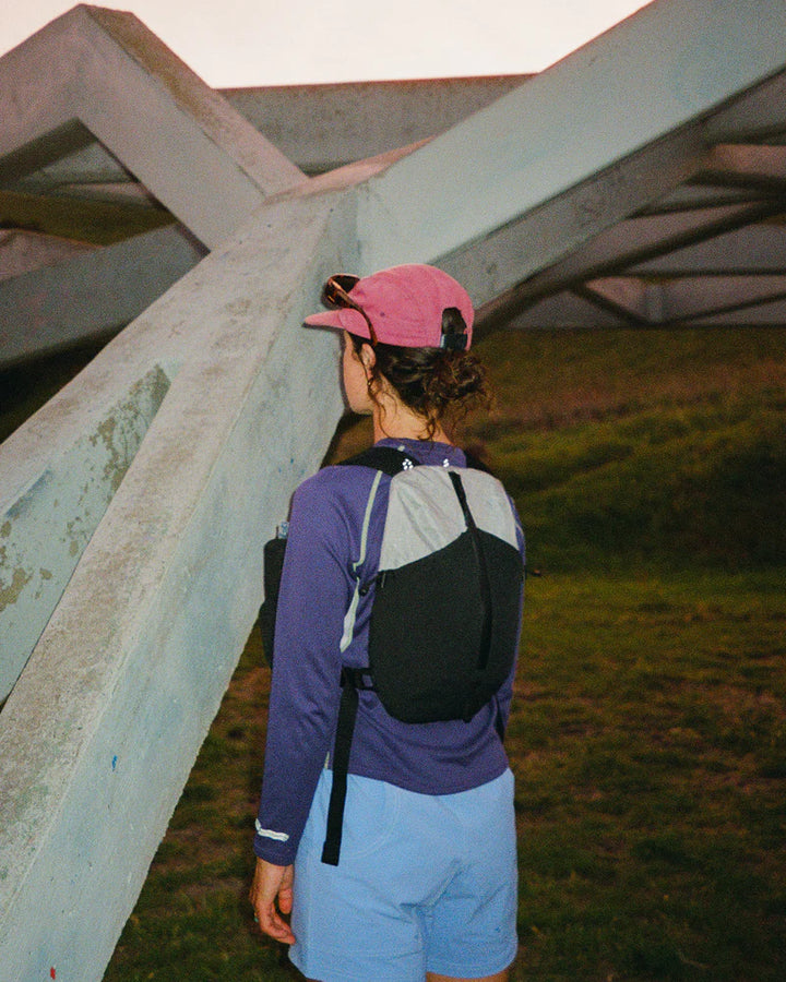 Person wearing a pink cap and carrying a black backpack under a concrete overpass.