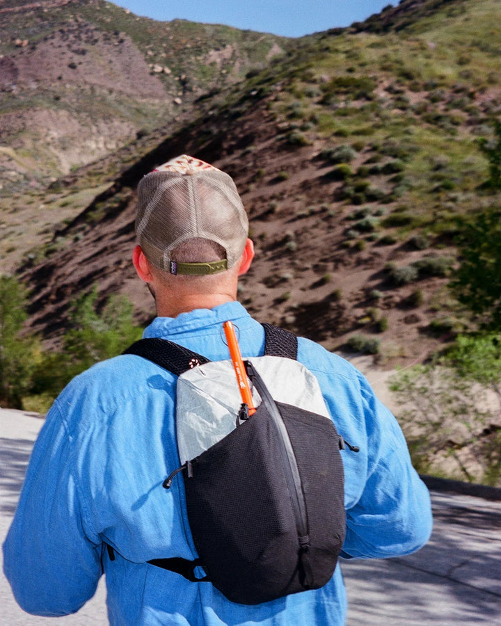 Person wearing a blue jacket and black backpack with a mountainous landscape in the background