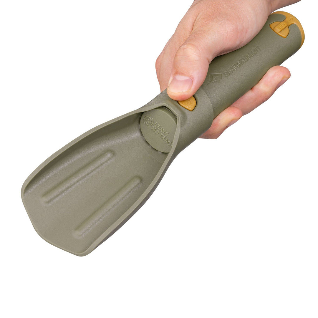 Hand holding a green plastic trowel against a white background