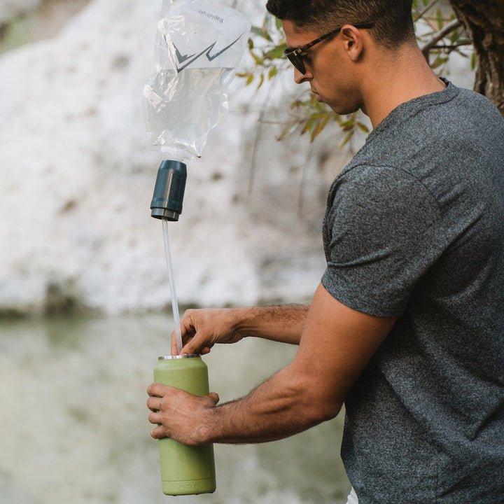 Person using a gravity fed water filtration system to fill a water bottle outdoors