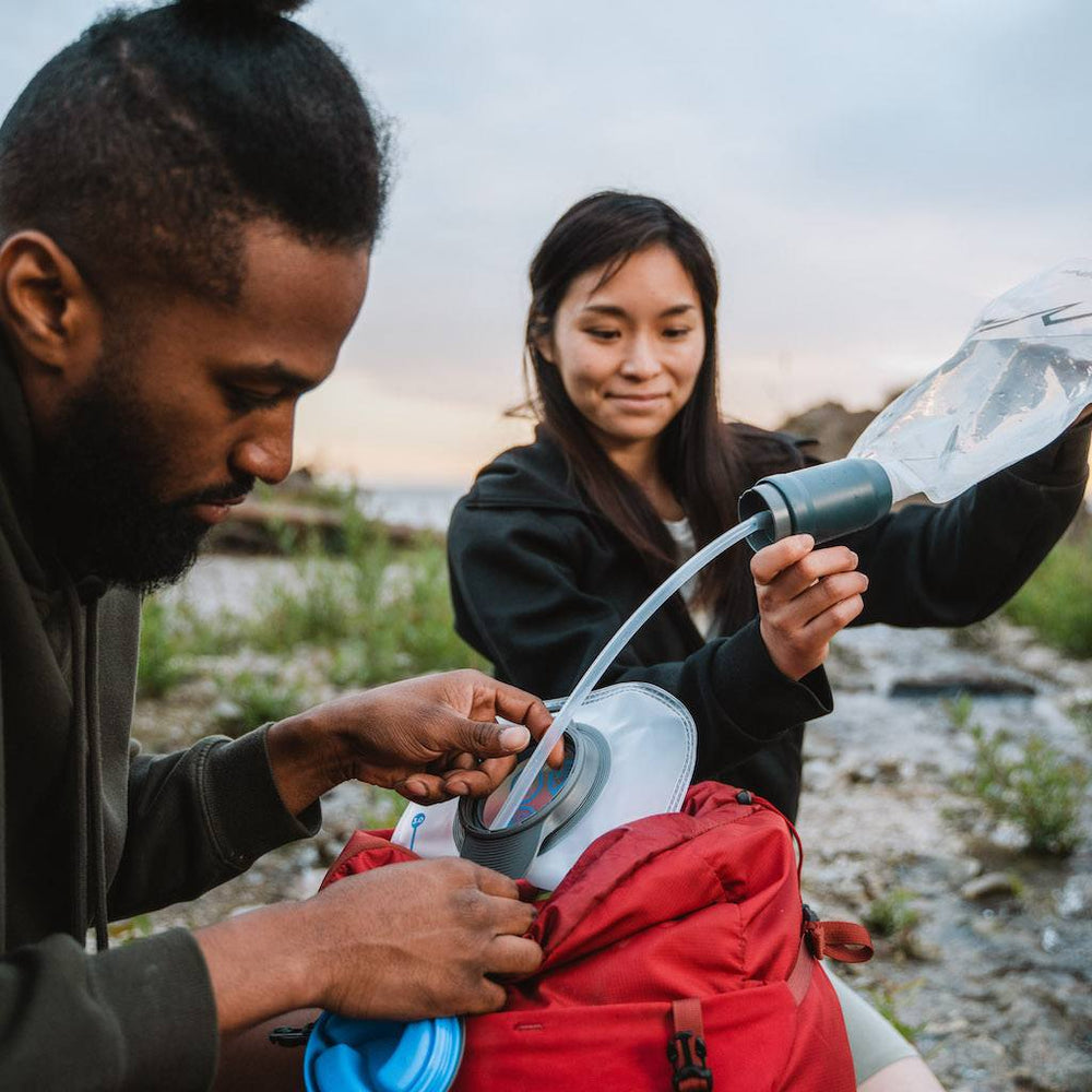 Two people using a water filter and soft bottle to fill a hydration bladder