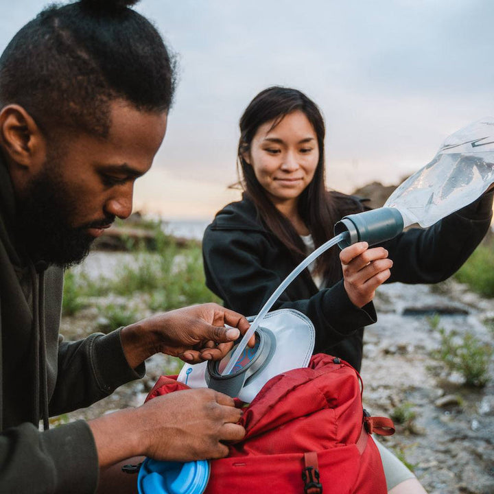 Two people using a water filter and soft bottle to fill a hydration bladder