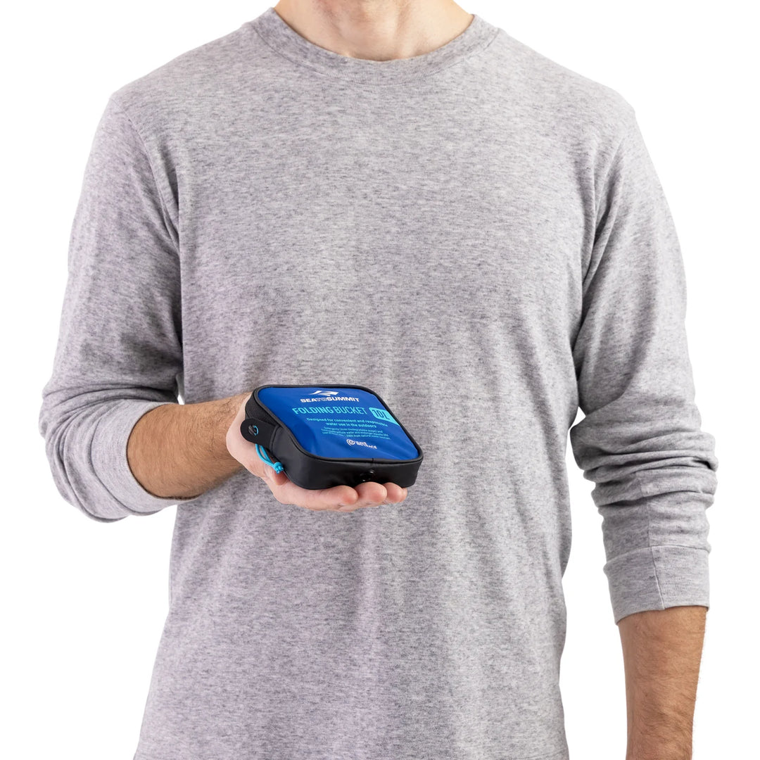 Person holding a blue packed up foldable bucket, wearing a gray long-sleeve shirt.