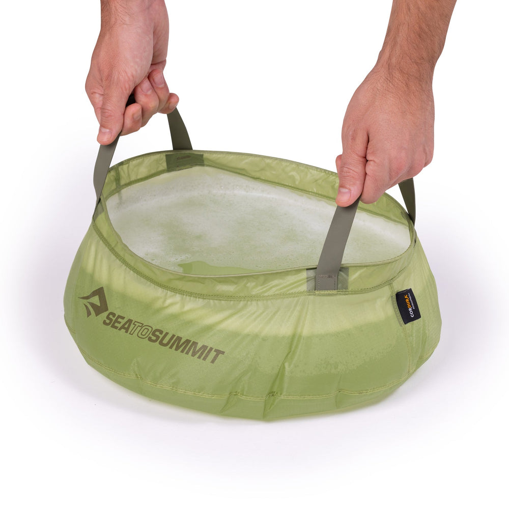 Green nylon washing-up sink being lifted by two hands on the two webbing side straps