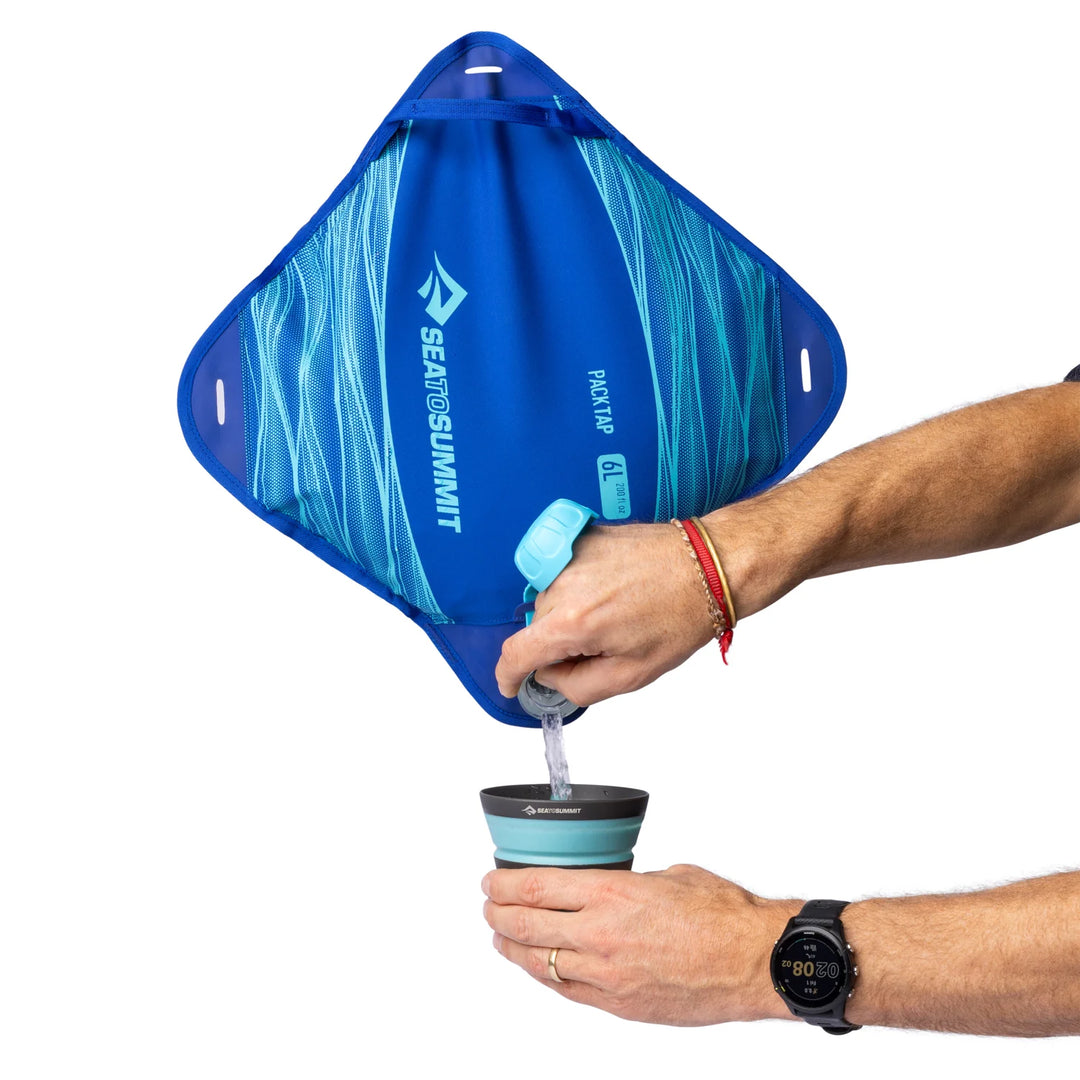Person using a blue Sea to Summit water filter bag to fill a cup with water.