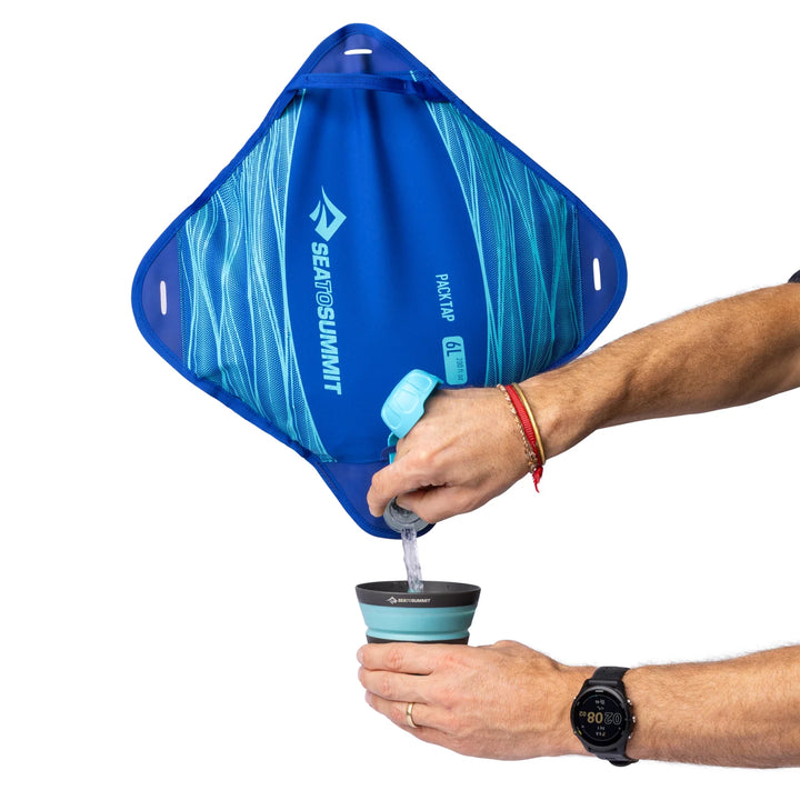Person using a blue Sea to Summit water filter bag to fill a cup with water.