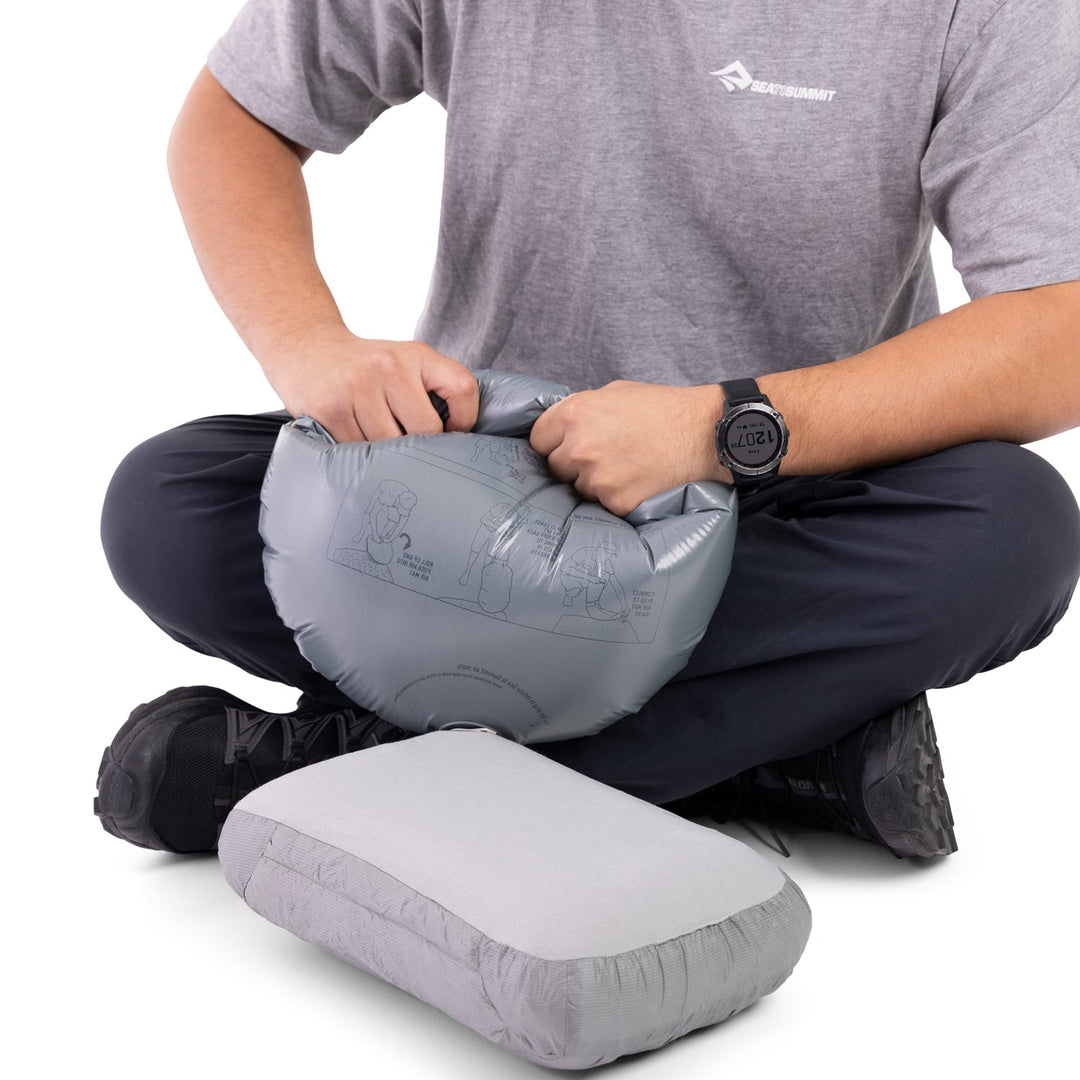 Person inflating a grey inflatable pillow with a grey pump sack