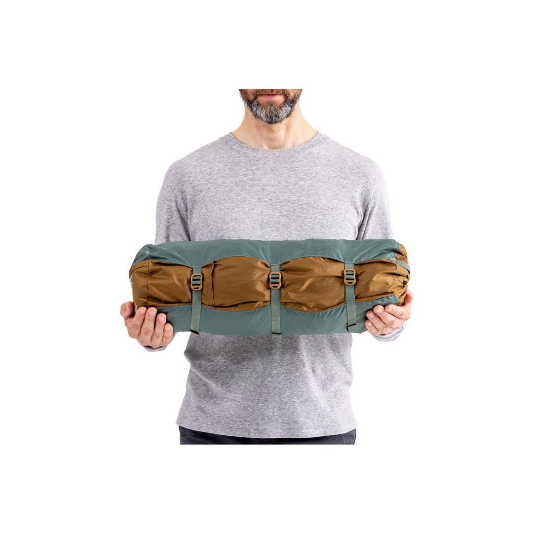 Man holding green and brown tent tent in its bag.