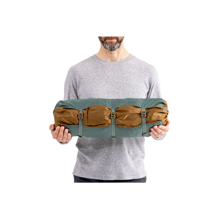 Man holding green and brown tent tent in its bag.