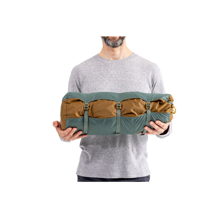 Man holding green and brown tent in its bag on a white background.