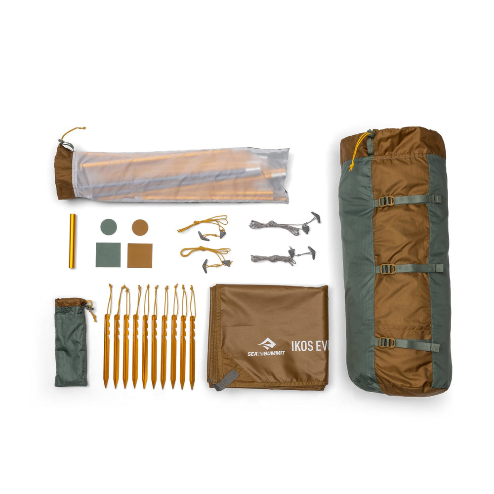 Green and brown tent in its bag along with a number of accessories arranged on a white background.