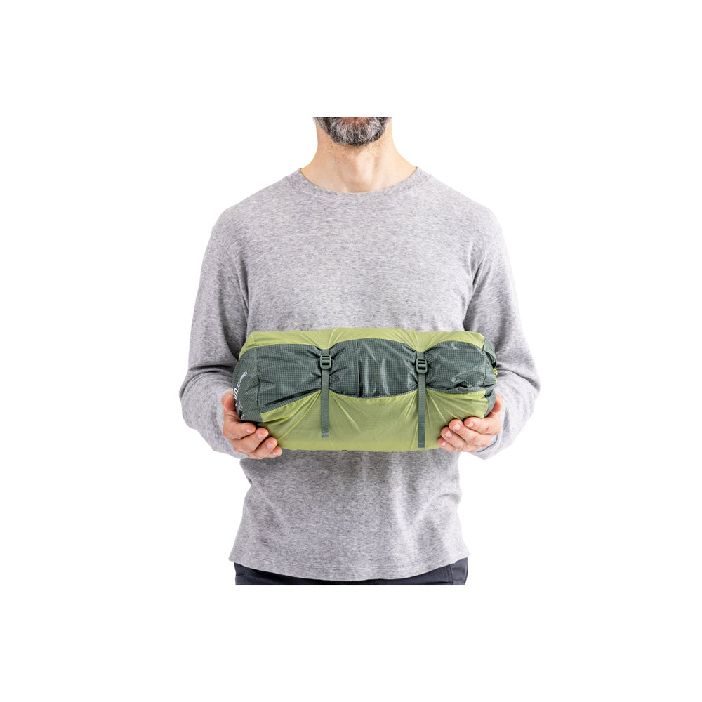 Man holding green and grey tent in its bag on a white background.