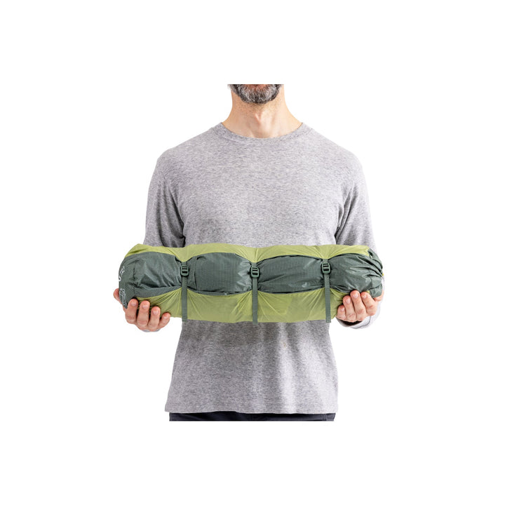 Man holding green and grey tent in its bag on a white background.