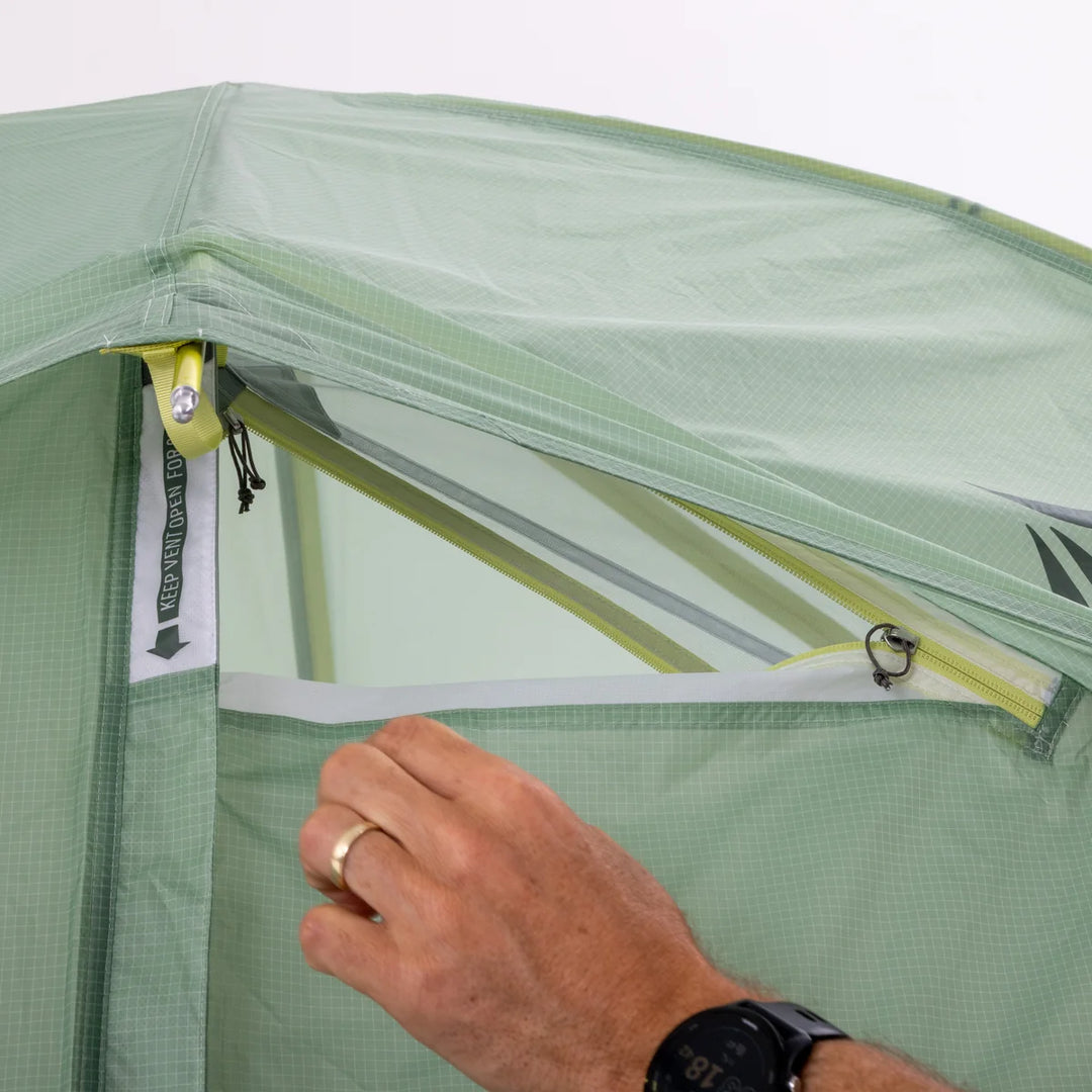 Person adjusting a green tent with a clear window, showing a close-up of the zipper.