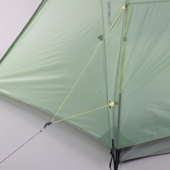 Close-up of a light green tent mesh fly with yellow guy lines and poles, shown against a plain light gray background.