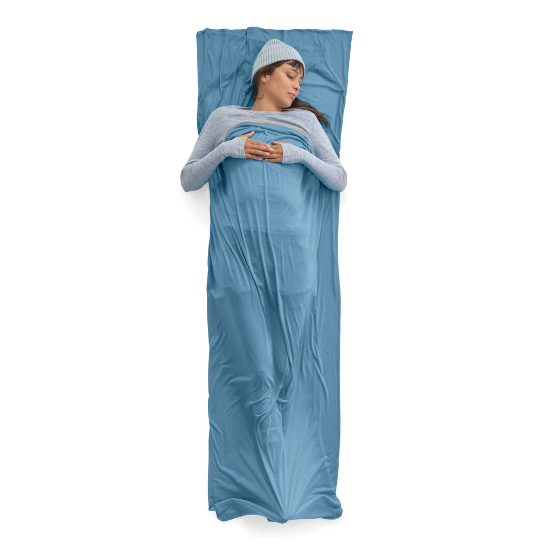 Person lying on a blue sleeping bag liner on a white background