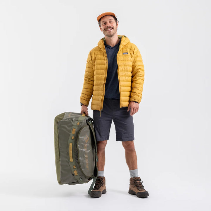 Man in yellow jacket holding a large green bag on a white background