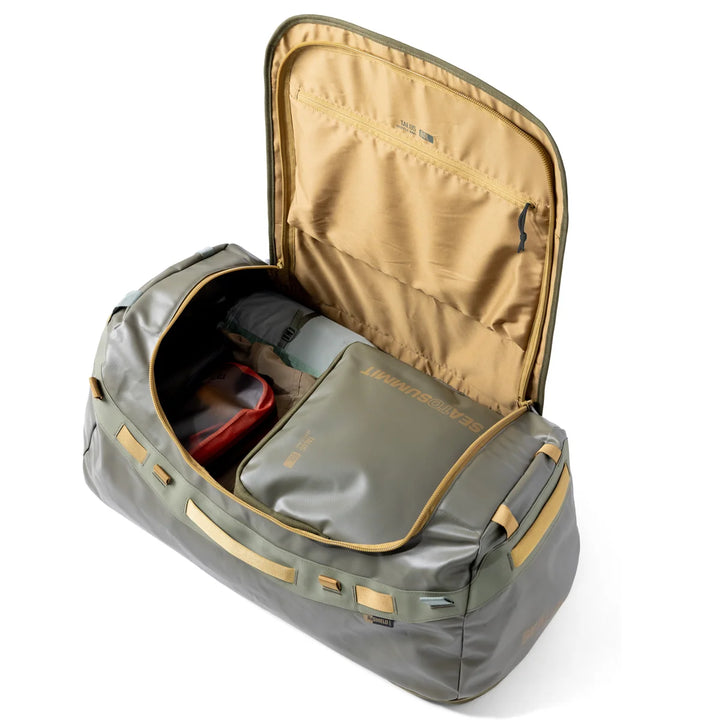 An olive green and tan packing cube shown open, filled with travel gear, on a clean white background.