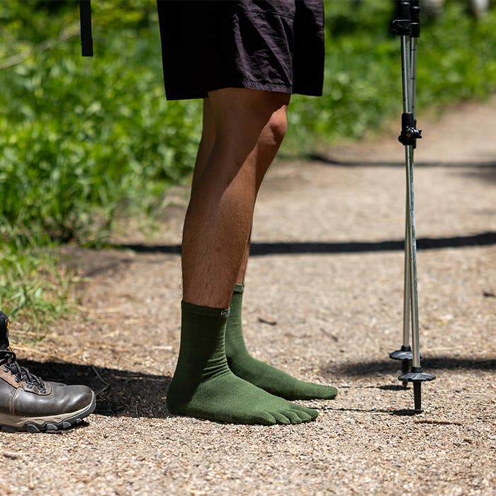 Person wearing green toe socks standing on a gravel path and holding trekking poles