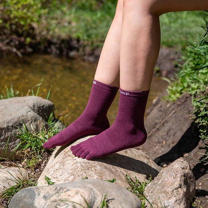Person wearing maroon toe socks sitting next to a stream with their feet on a rock