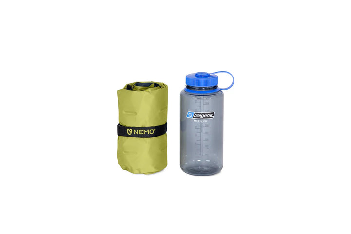 Packed up green Nemo sleeping mat sitting beside Nalgene water bottle on a white background.