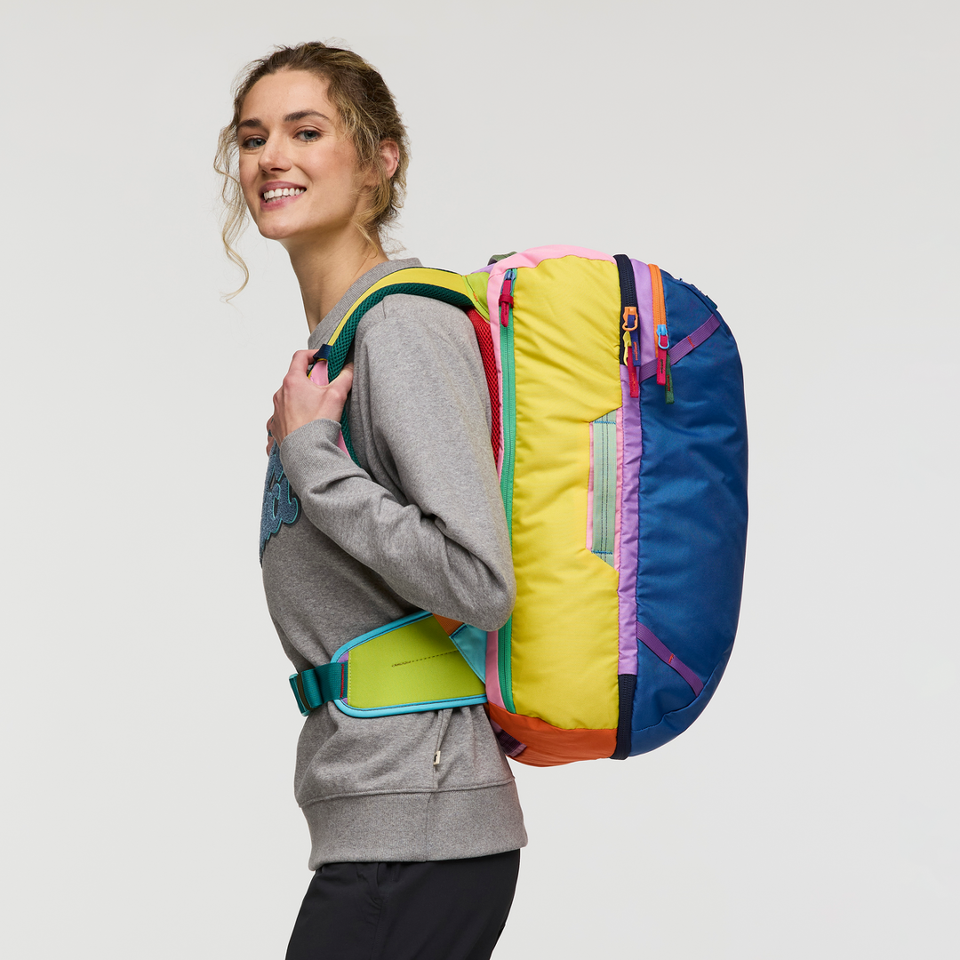 Woman in profile, wearing a colourful backpack on a white background and smiling at the camera