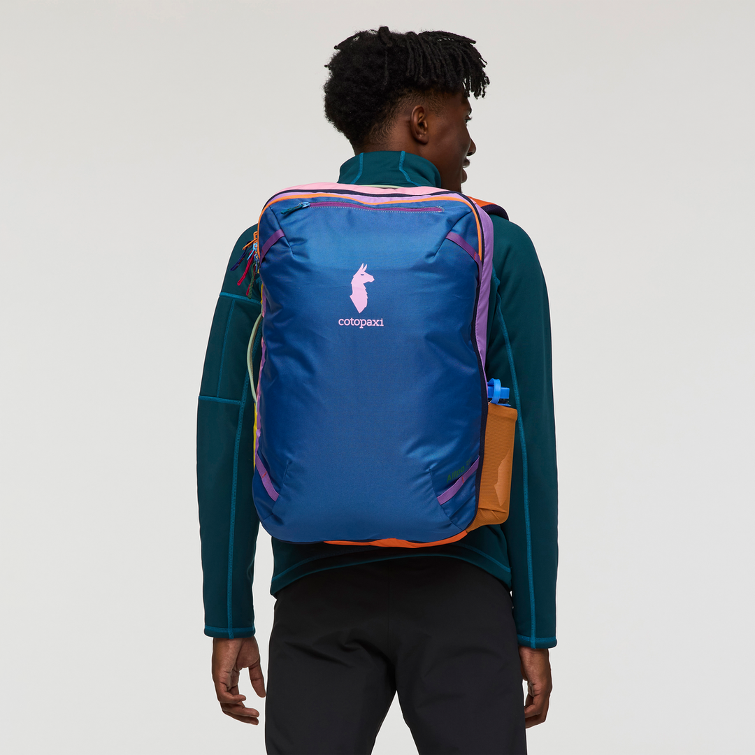 Man wearing a colourful backpack with the Cotopaxi logo on a white background