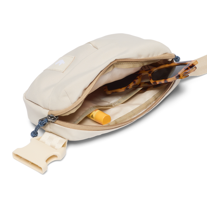 Beige crossbody bag with sunglasses and a bottle inside on a white background