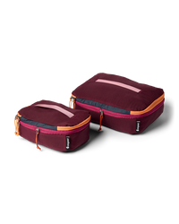 Two maroon travel packing cubes with orange zippers on a white background