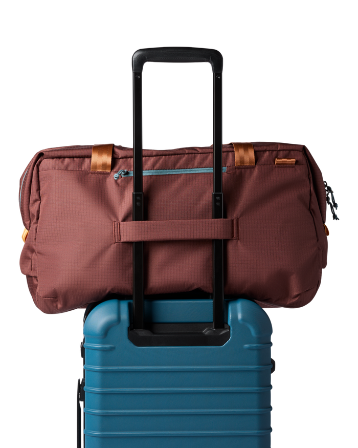 Brown duffel bag on top of a blue suitcase with a white background