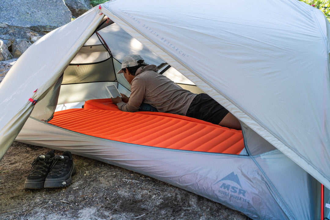 Person lying on an orange sleeping pad inside a white tent with &