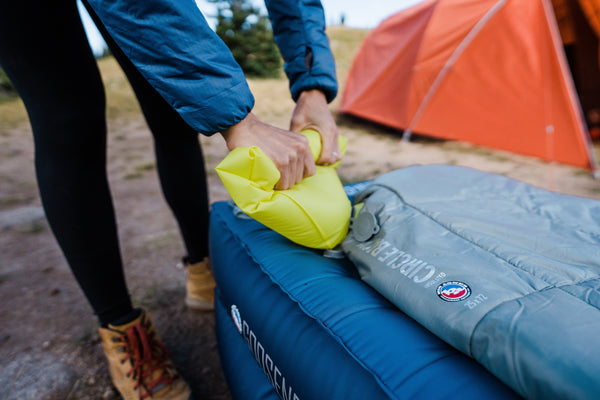 Person setting up camping gear with a sleeping bag and tent in the background