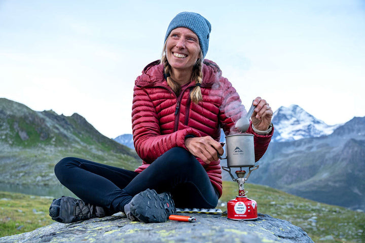 Person sitting on a rock with a camping stove in a mountainous landscape