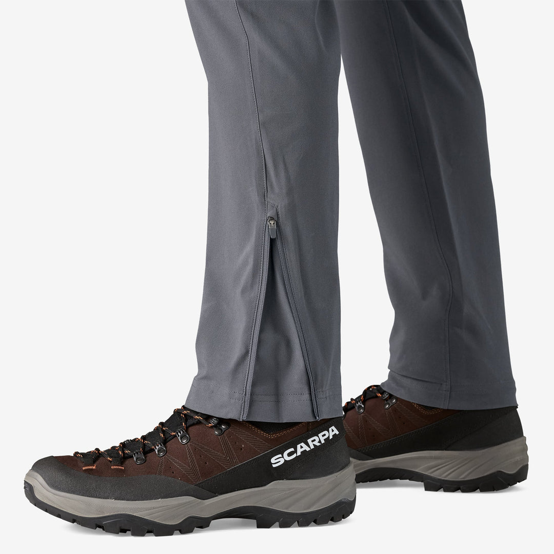 Close up of the feet of a person wearing grey pants and hiking boots showing a zip on the cuff of the pants