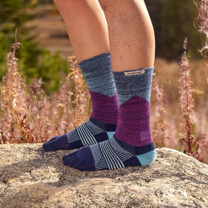 Person wearing blue and purple patterned  socks on a rock with a natural background