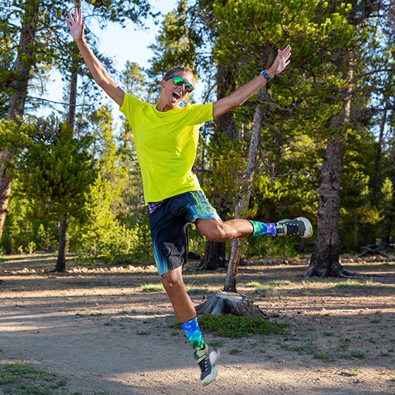Person in a bright yellow shirt and colorful socks jumping in a forest