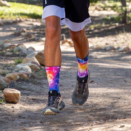 Person wearing colorful tie-dye socks captured mid-stride on a trail run