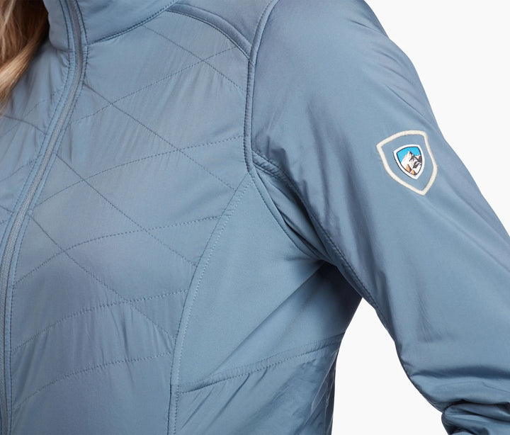 The shoulder of a light blue quilted jacket with the Kuhl logo on the shoulder