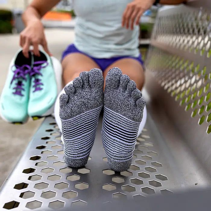 Person wearing toe-separated socks sitting on a metal bench.