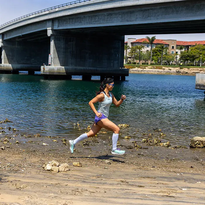 Woman running along a path by a body of water with a bridge in the background