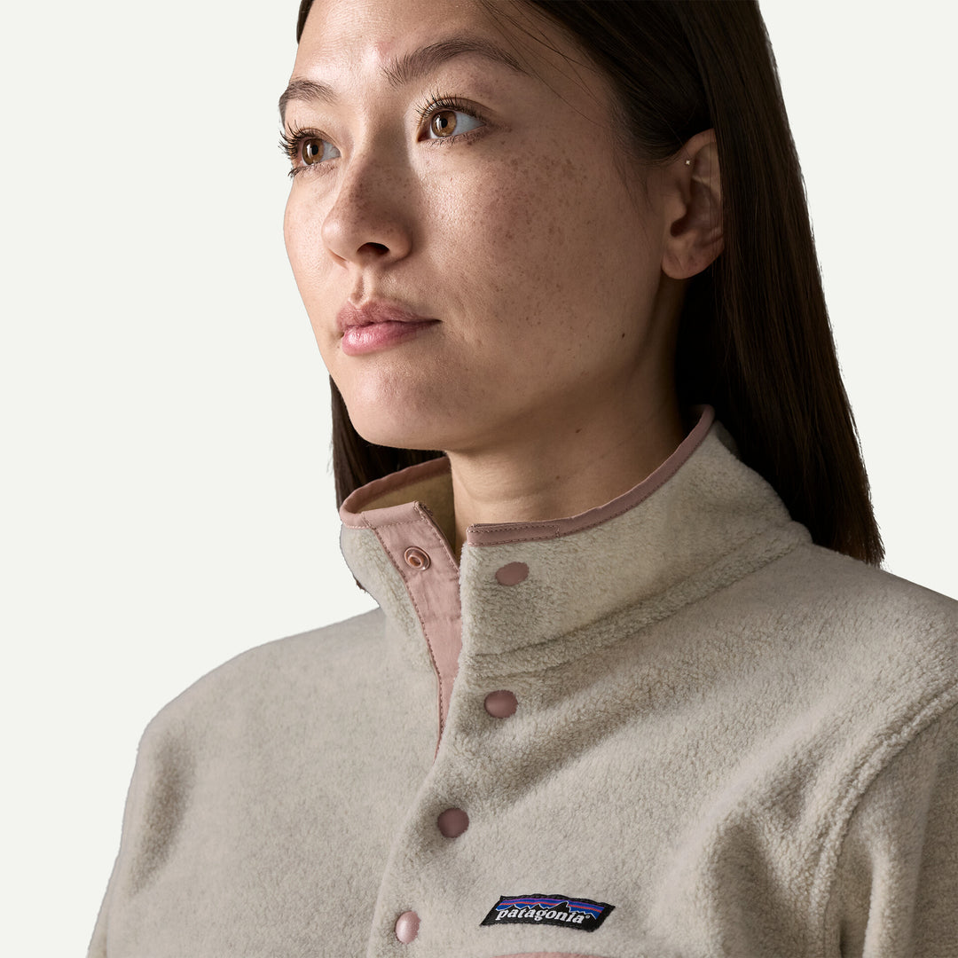 Close-up of a woman wearing a light beige Patagonia fleece pullover with a pink inner collar and matching pink buttons, shown against a plain off-white background.