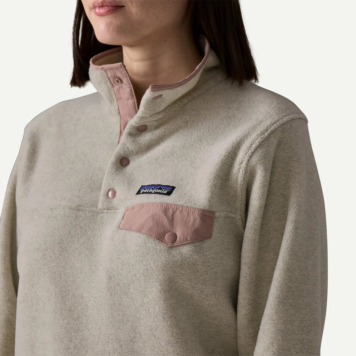 Close-up of a person wearing a Patagonia fleece pullover in a light oatmeal beige color with a muted dusty pink pocket and button placket.