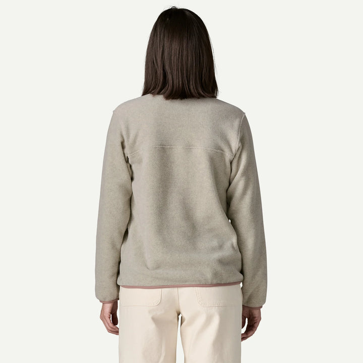 A woman viewed from the back wearing a light beige fleece sweater and cream pants against a plain off-white studio background.