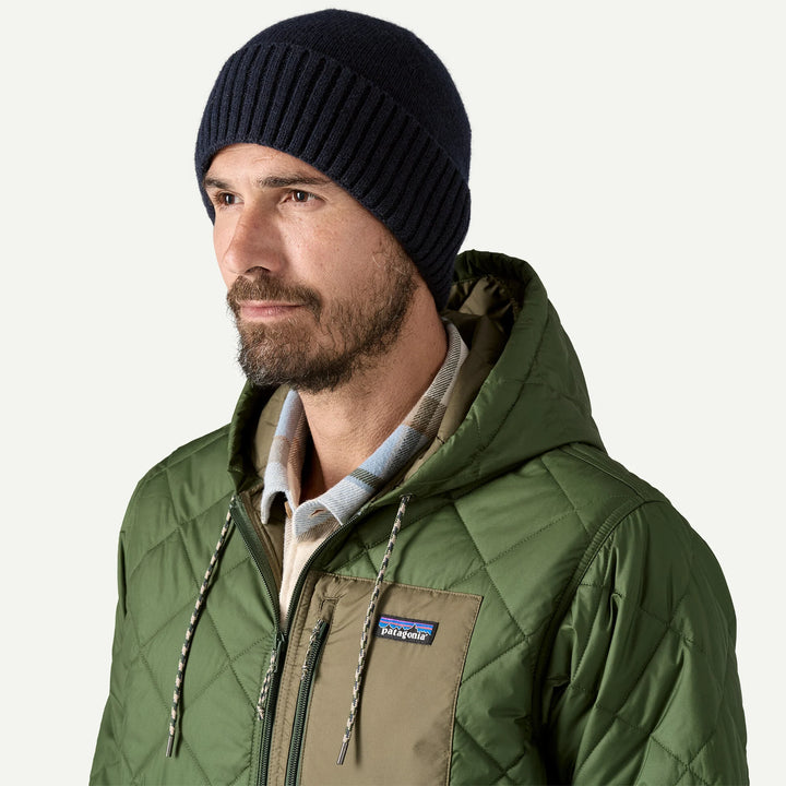 Man wearing a green quilted jacket with a Patagonia logo and a black beanie on a white background