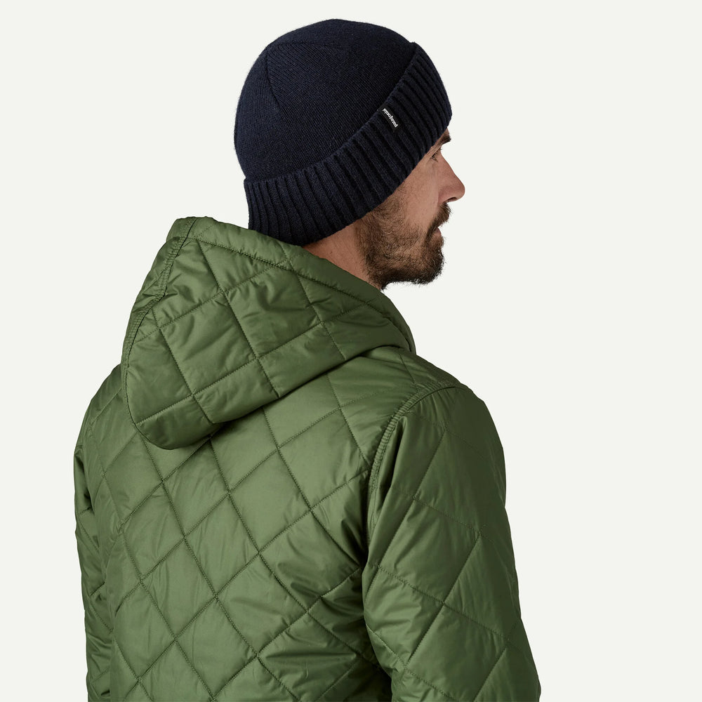 Man wearing a green quilted jacket and navy beanie on a white background