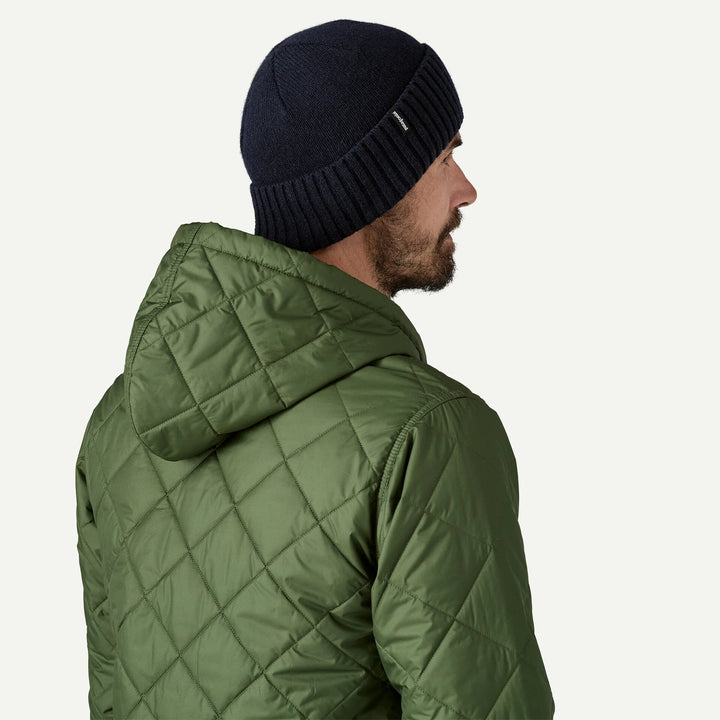 Man wearing a green quilted jacket and navy beanie on a white background