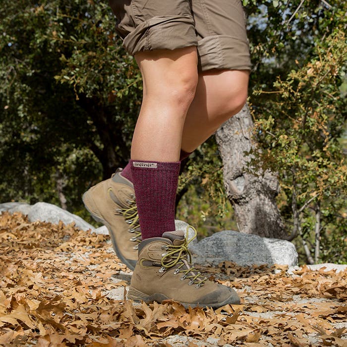 Person wearing hiking boots and Injinji Hiker + Liner combo socks with a brand logo, standing on leaf-covered ground.