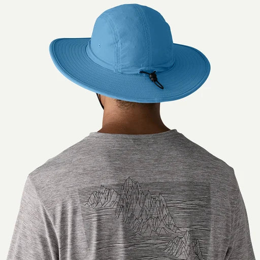 Person wearing a blue wide-brimmed hat and a gray t-shirt with mountain design on a white background
