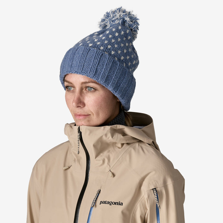 Woman wearing a blue knit beanie with a pom-pom and a beige Patagonia jacket on a white background